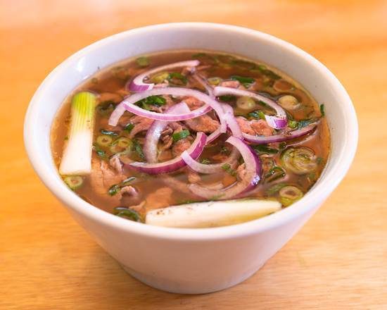 A bowl of pho with sliced red onion, spring onion and herbs