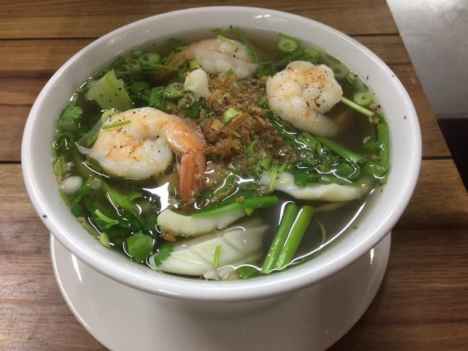 A bowl of soup with prawns, greens and fried shallots